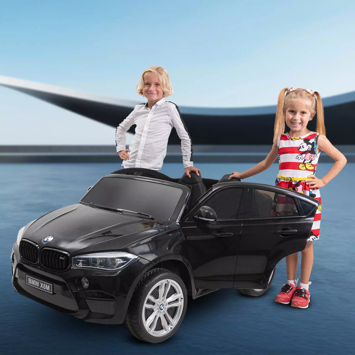 Bruder und Schwester stehen lächelnd neben dem schwarzen BMW Kinderauto