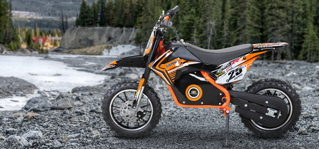 Schwarz-orangefarbenes Elektro-Kindermotorrad auf nassem Kiesuntergrund