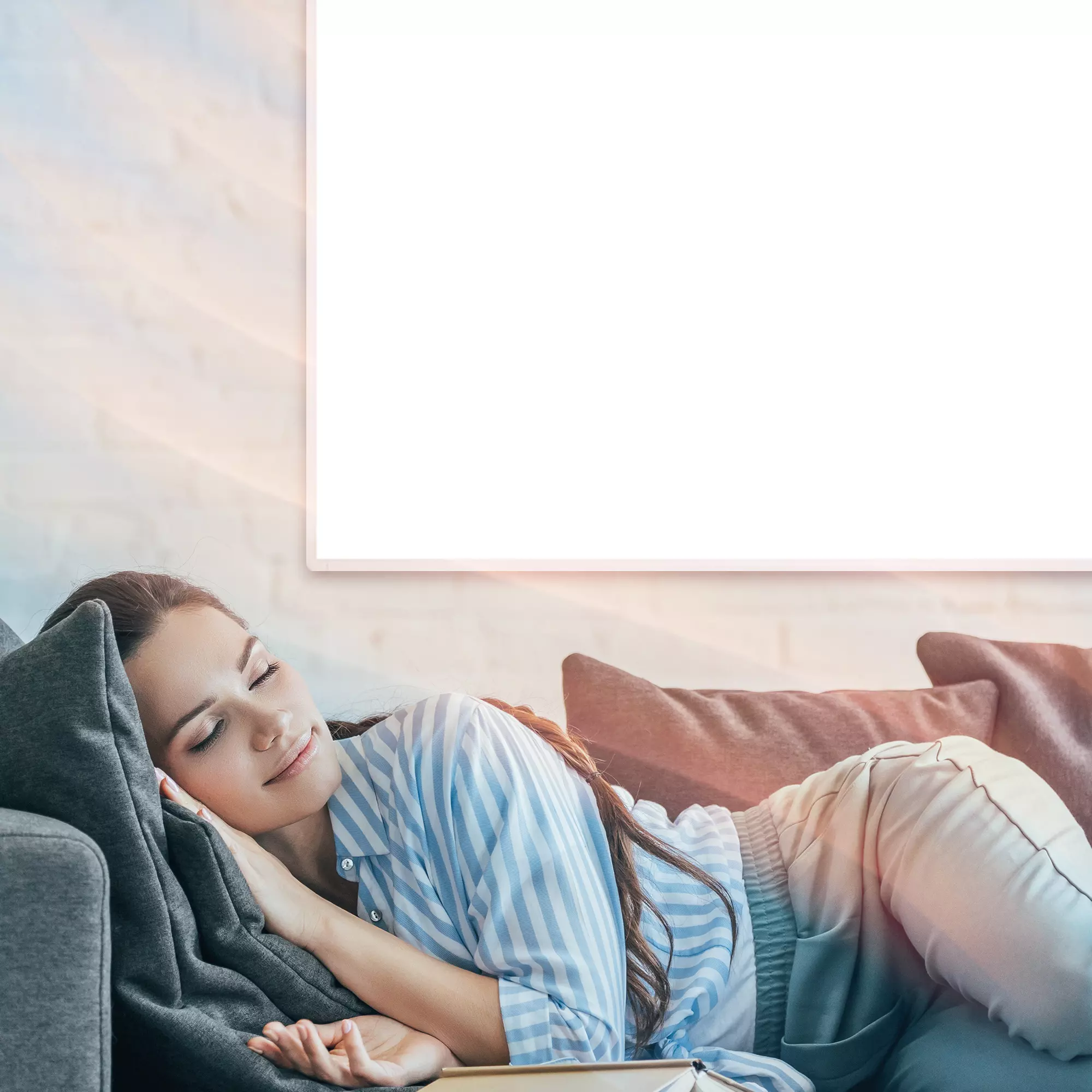 Frau schläft auf Couch und genießt Wärme des an der Wand befestigten Infrarotheizkörpers