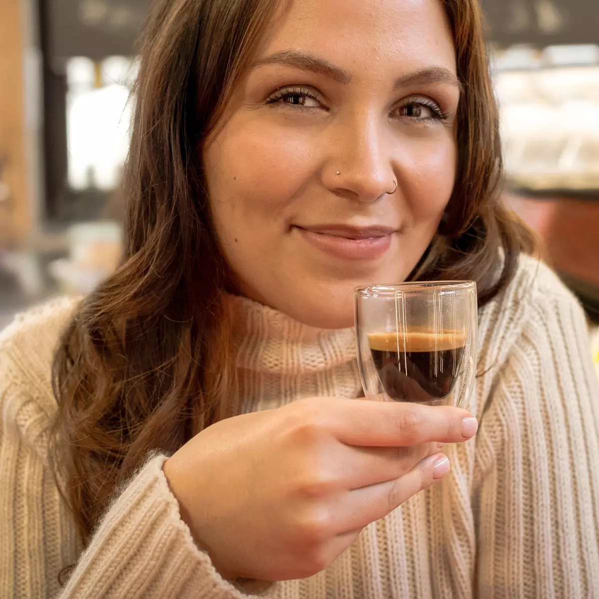 Frau hält lächelnd das Königsglas in der Hand und genießt den Espresso